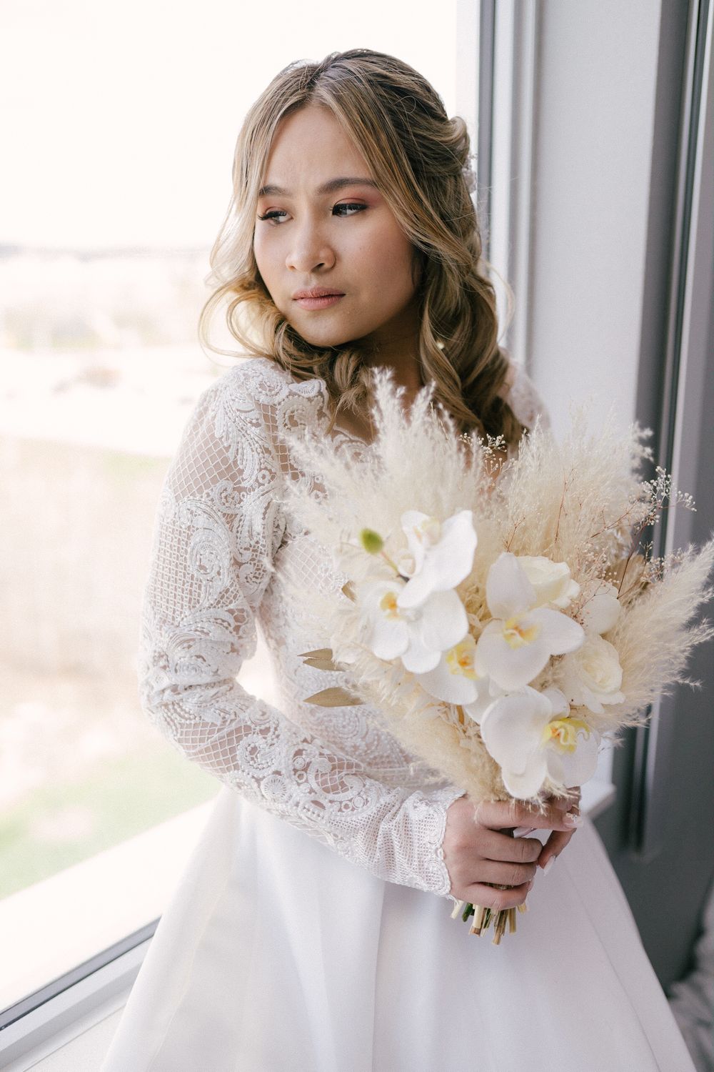 Bride holding a white orchid bouquet beside a window