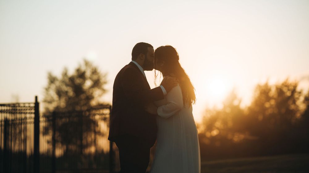 Newlyweds kissing in silhouette at sunset
